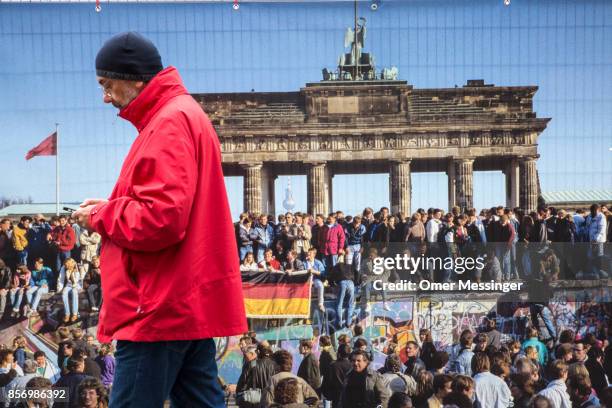 Man is passing by a poster with a seen from ttthe fall of the Berlin Wall at the entrance to an amusement area set up along 17th of June Street in...