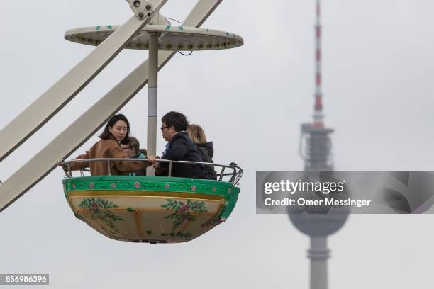 People take a ride in a fairies wttheel as Berlin's TV Tower is seen in the background, at an amusement area set up along 17th of June Street in...