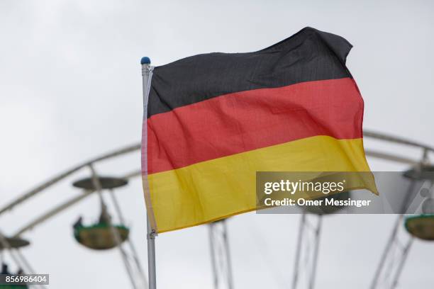 Ttthe German national flag is seen in front of a ferris wheel near an amusement area set up along 17th of June Street in Tiergarten Park near the...