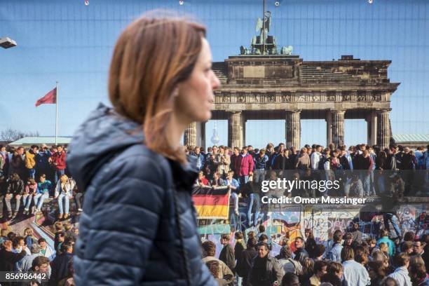 Woman is passing by a poster with a seen from ttthe fall of the Berlin Wall at the entrance to an amusement area set up along 17th of June Street in...