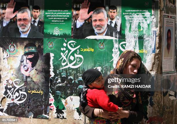 Palestinian woman carries her son as she walks past portraits of Hamas leader Ismail Haniya at the Palestinian refugees camp of Shatila in the...