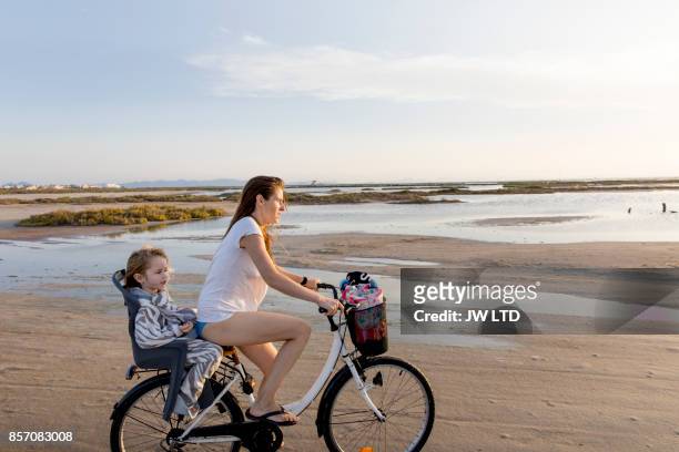 mother and daughter cycling on the beach - fahrradsattel stock-fotos und bilder