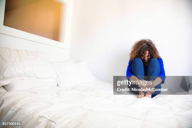 distressed mature caucasian female sitting on her bed in fetal position - fetal position stock pictures, royalty-free photos & images