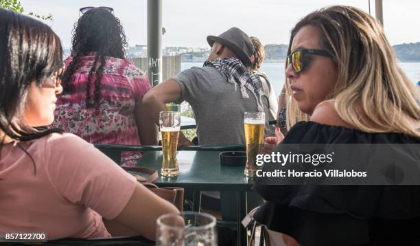 Tourists drink Super Bock draught beer at a terrace bar in the viewpoint of Santa Catarina, a spot favored by visitors, on October 01, 2017 in...