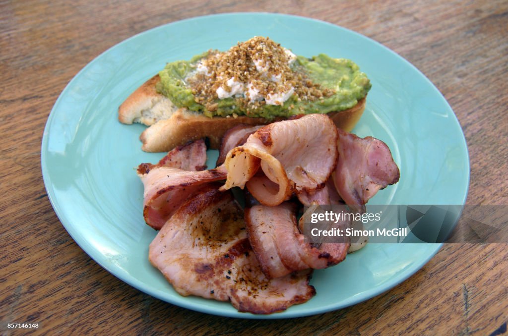 Smashed avocado, crumbled feta cheese and dukkah on toasted sourdough bread with a side of fried bacon