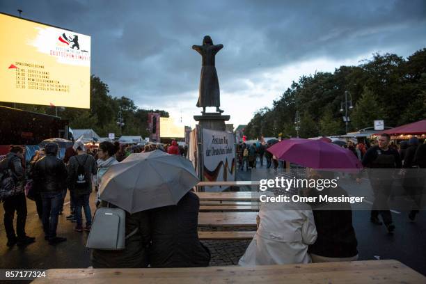 People sit in under umbrellas at an amusement area set up along 17th of June Street in Tiergraten Park near the Brandenburg Gate on German Unity Day...