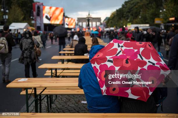 People sit under open umbrellas at an amusement area set up along 17th of June Street in Tiergraten Park near the Brandenburg Gate on German Unity...
