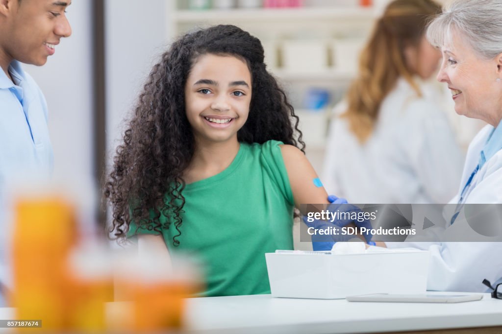 Preteen girl smiles for camera after flu vaccination at pharmacy