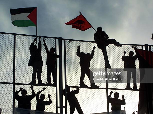 Palestinian boys climb a fence for a better view of gunmen marching during a protest against Israel March 1, 2002 in the Rafah refugee camp in the...