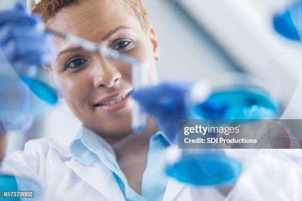 view from below of beautiful lab technician adding solution to test tube - black scientists stock pictures, royalty-free photos & images