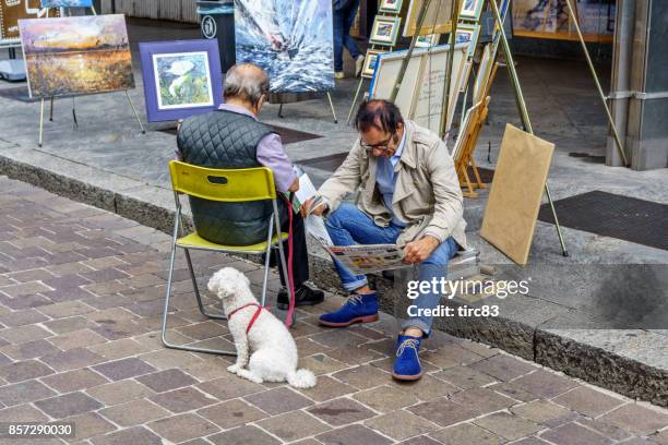 escena de la calle como. dos hombres maduros con un perro sentado en el bordillo - kerb fotografías e imágenes de stock