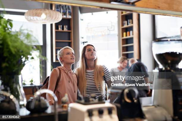 two young women looking up at menu board in café - bar man t shirt stock-fotos und bilder