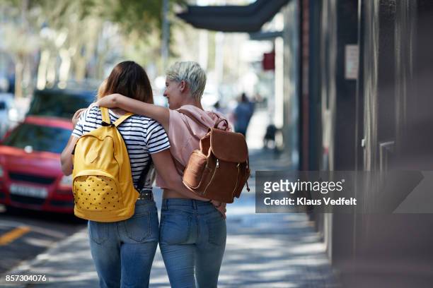 Two young women walking arm in arm, down street