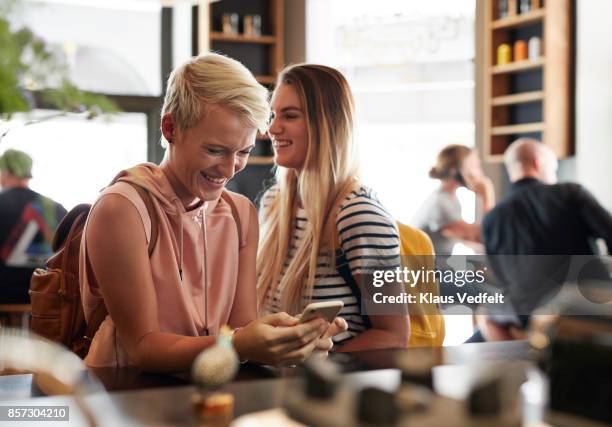 young woman standing in café and laughing while looking at phone - coffee shop friends stock-fotos und bilder