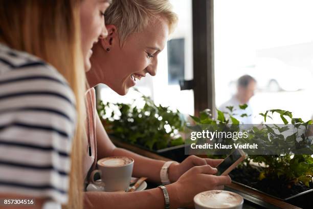 Two young women looking at phone together, at café