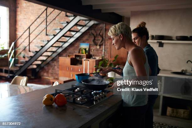 two young women cooking together in loft apartment - hot wife stockfoto's en -beelden