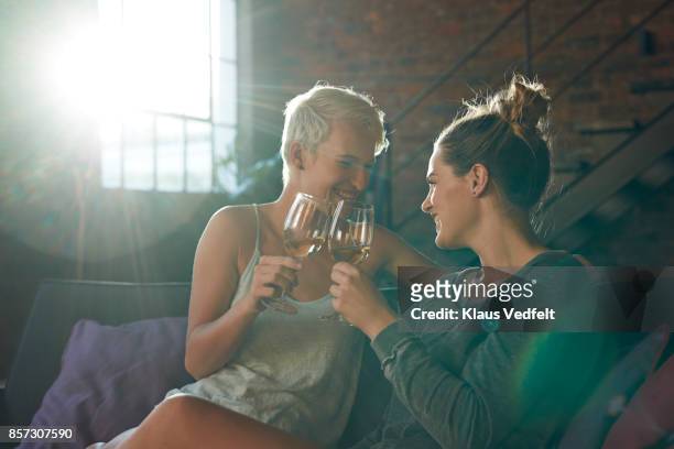 Lesbian couple sitting in sofa, toasting wine