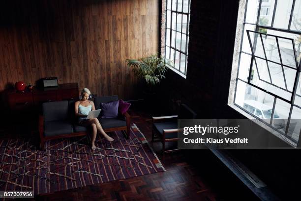 woman looking at laptop, while sitting in sofa - loft interior photos et images de collection