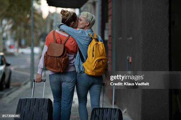 lesbian couple walking together with rolling suitcases - couple jeans shirt stock-fotos und bilder