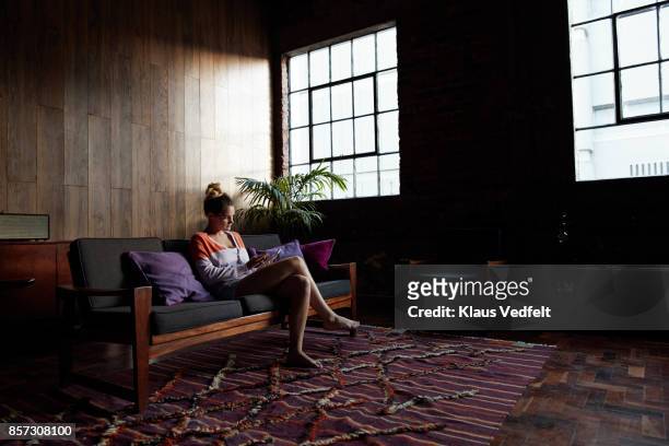 young woman sitting in couch and using digital tablet - get out film 2017 stock pictures, royalty-free photos & images