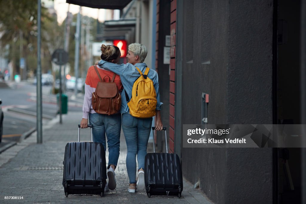 Lesbian couple walking together with rolling suitcases