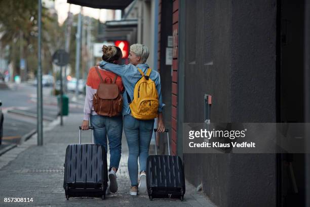 Lesbian couple walking together with rolling suitcases