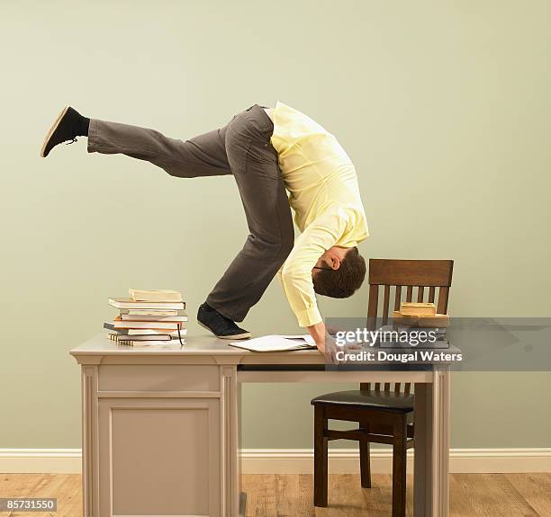 young man performing forward roll on desk. - somersault stock pictures, royalty-free photos & images