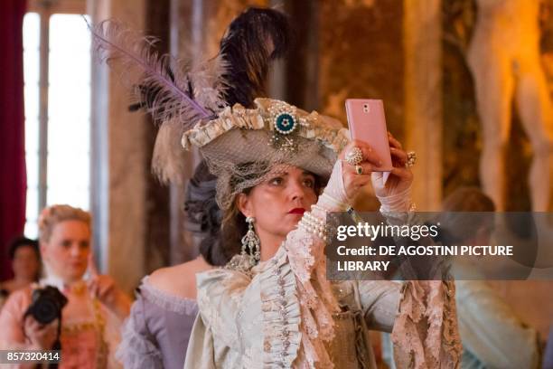 Lady wearing a hat and taking a selfie with a smartphone, courtship party with participants wearing clothes from the Louis XIV period, Palace of...