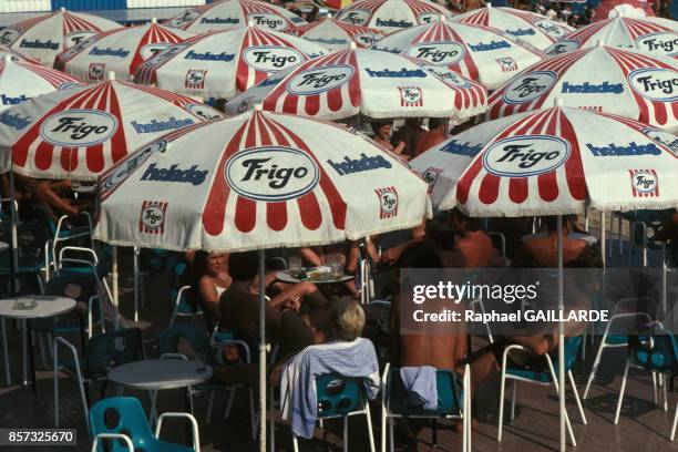 Consommateurs a la terrasse d'un cafe abrites du soleil par de nombreux parasols en mai 1992 a Tossa De Mar, Espagne.