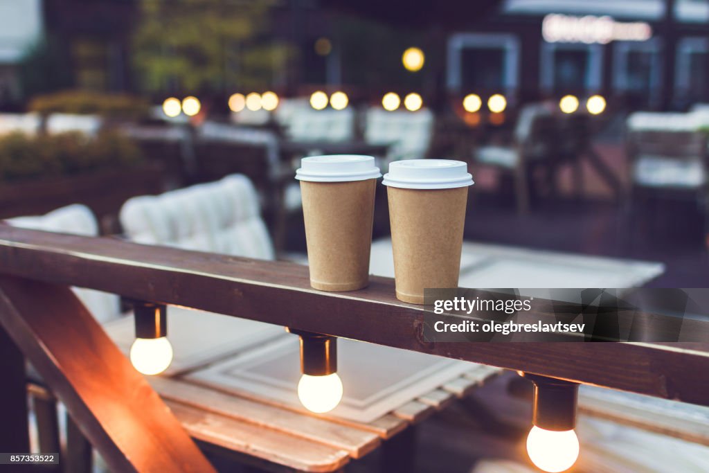 Två koppar takeaway kaffe på café veranda med bokeh lampor