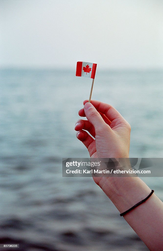 Human hand holding Canadian flag in front of lake