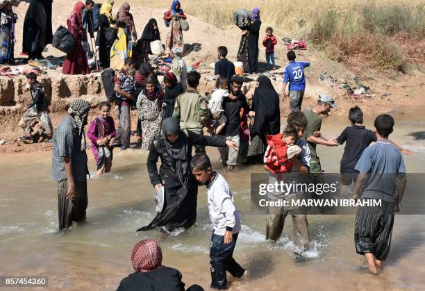 Displaced Iraqis who fled from the ongoing battles to oust the Islamic State group from Hawija, cross a river in the area of Zarga some 35 kilometres...