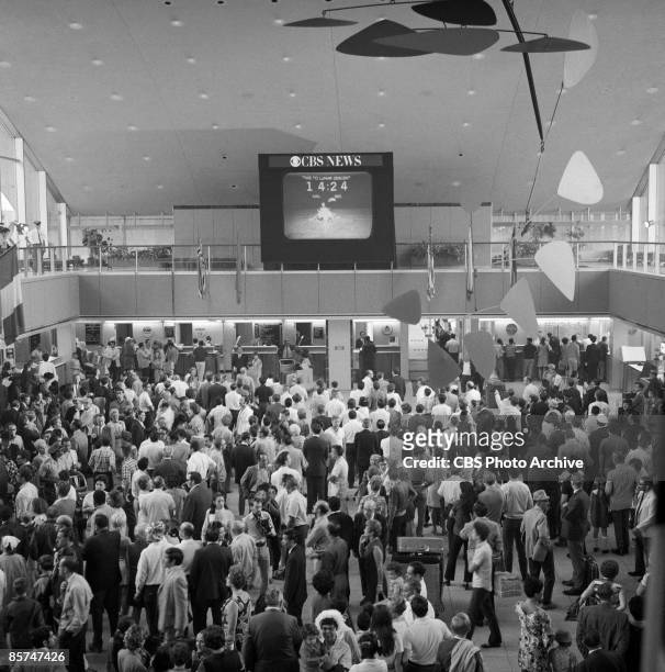 High-angle interior view of the International Arrival Building at John F. Kennedy International Airport shows a crowd of passengers as they stand...