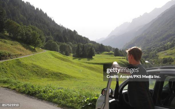 young man pauses by roadside, mountain valley - parked cars stock pictures, royalty-free photos & images