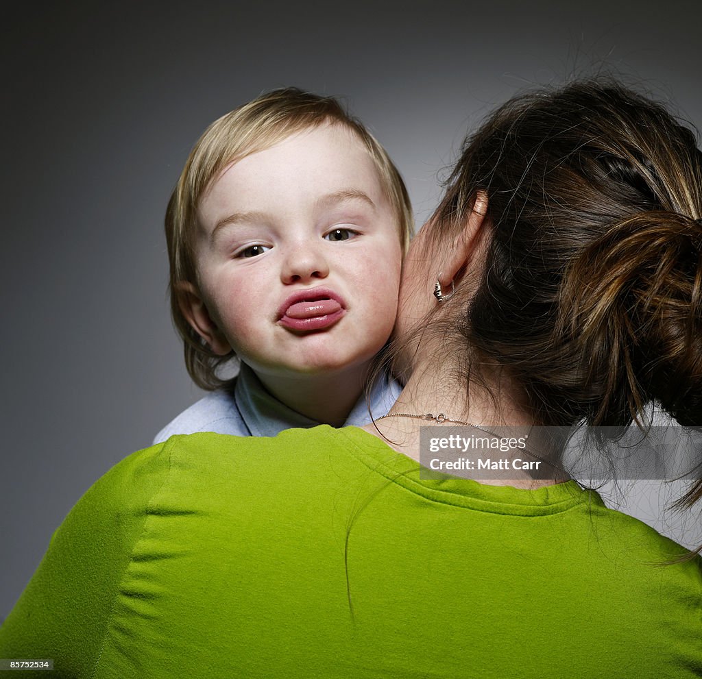 Young Boy making faces on mom's shoulder