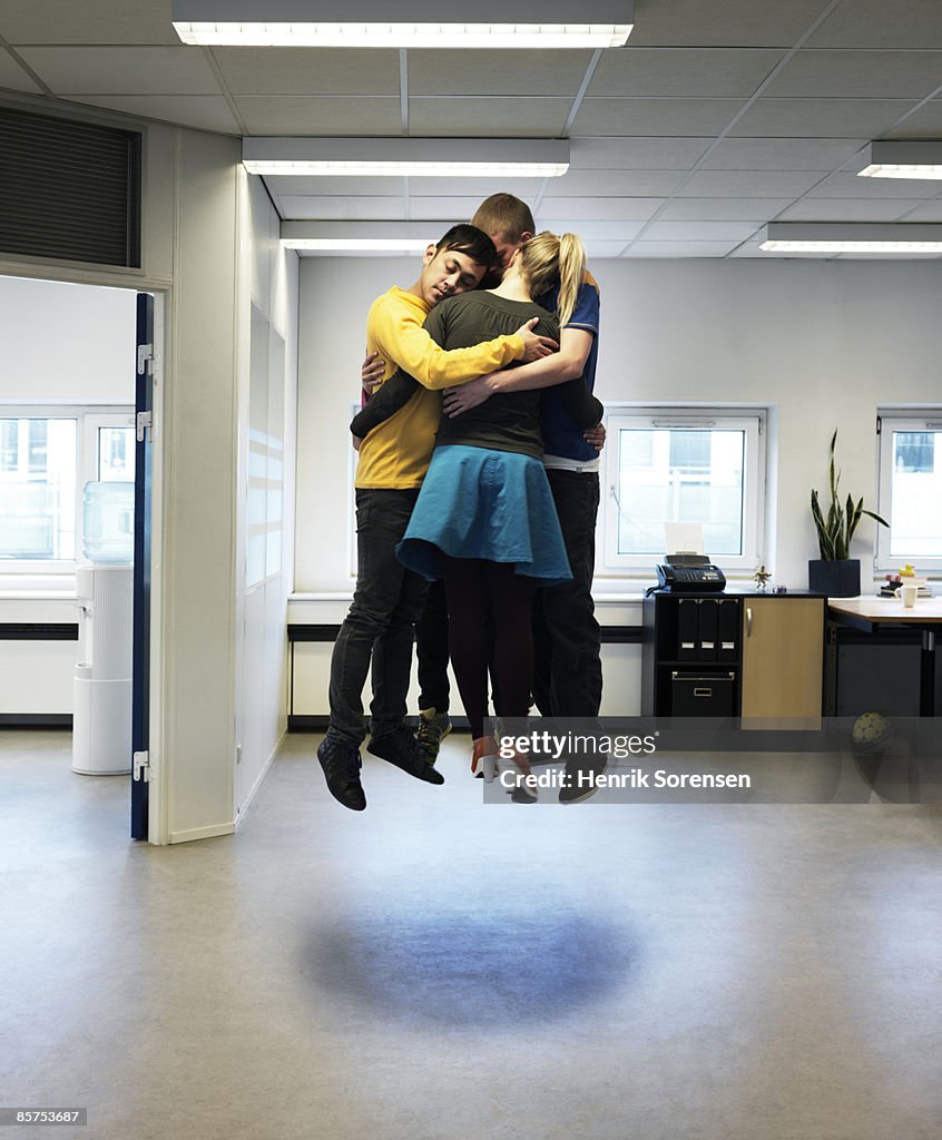 4 people in an office hugging and floating above t