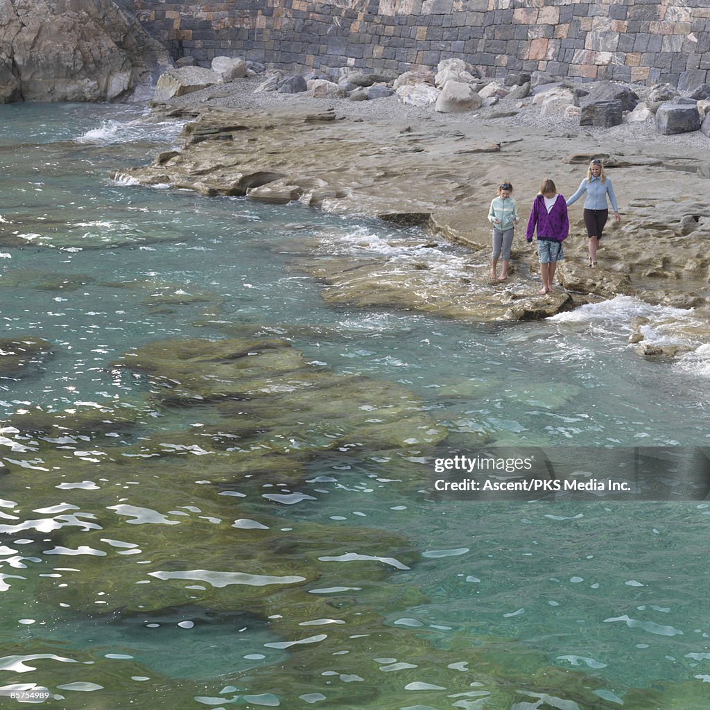 Family walk along edge of sea below rock wall