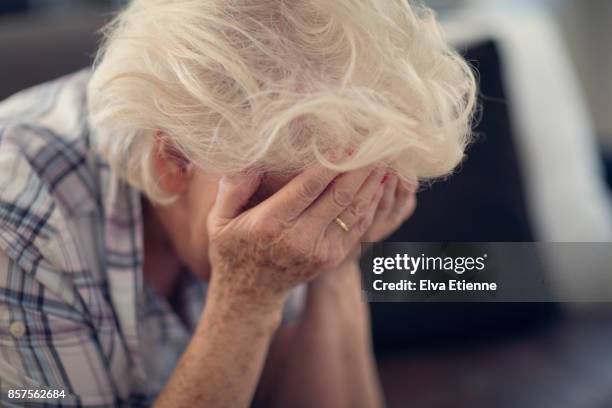 senior woman holding head in hands in despair - donne anziane foto e immagini stock