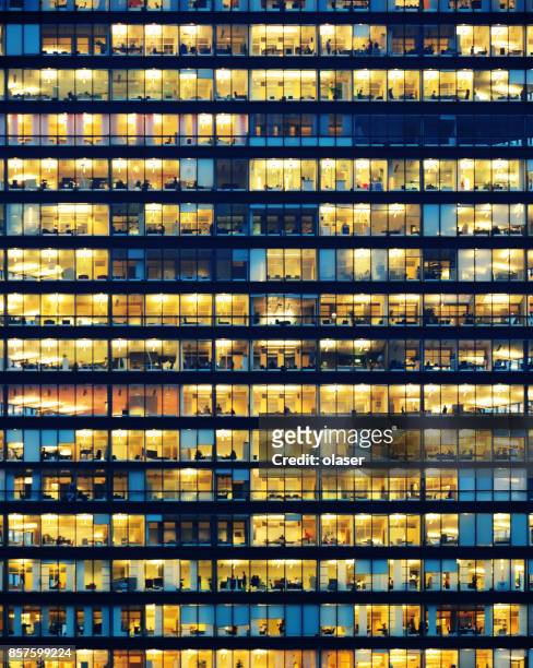 office workers working late in major office building - facade stock pictures, royalty-free photos & images