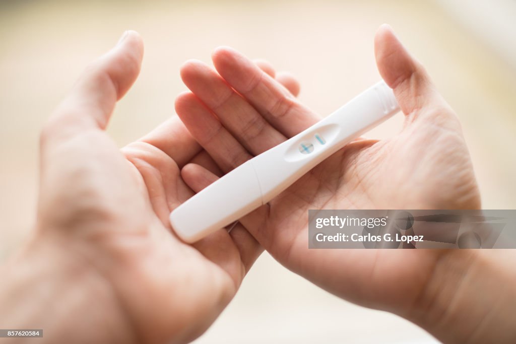 A man and a woman's hands holding together a pregnancy test revealing the positive outcome - Pregnancy/Birth