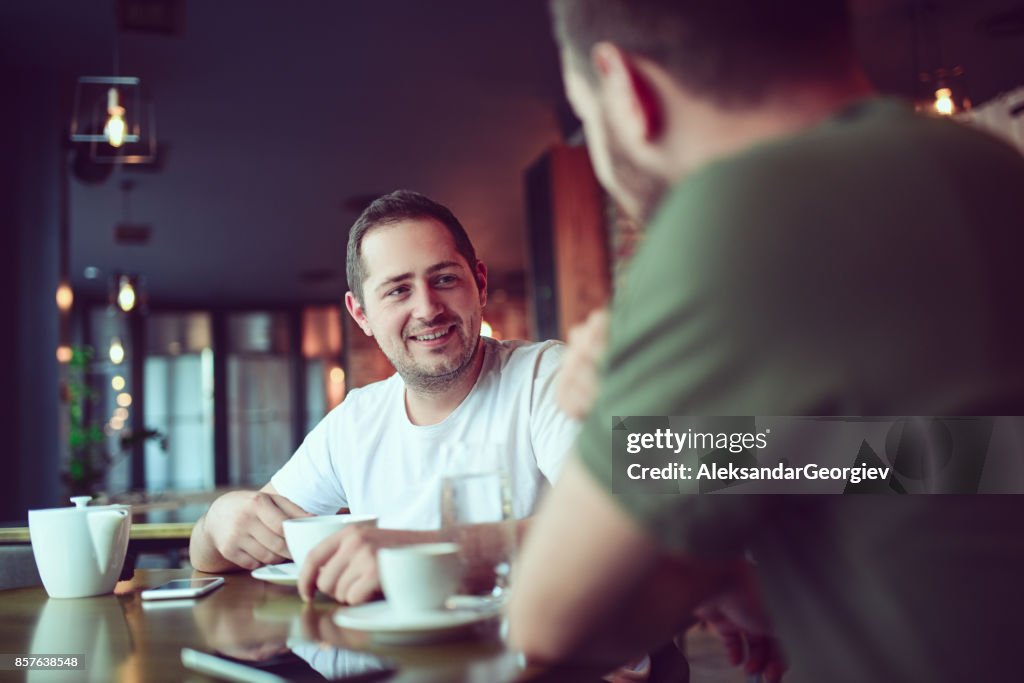 Two Smiling Friends Drinking Coffee and Socialising in a Cafe