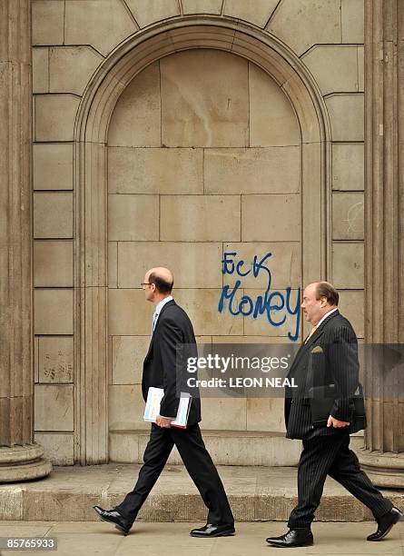 City workers walk past grafitti left by protestors on a wall of the Bank of England in central London, on April 2, 2009. Angry protestors clashed...
