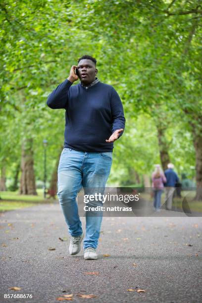 young black male walking in the park on his mobile phone - funky boy stock pictures, royalty-free photos & images