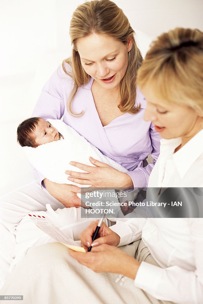 Health visitor filling out form for mother holding new born baby