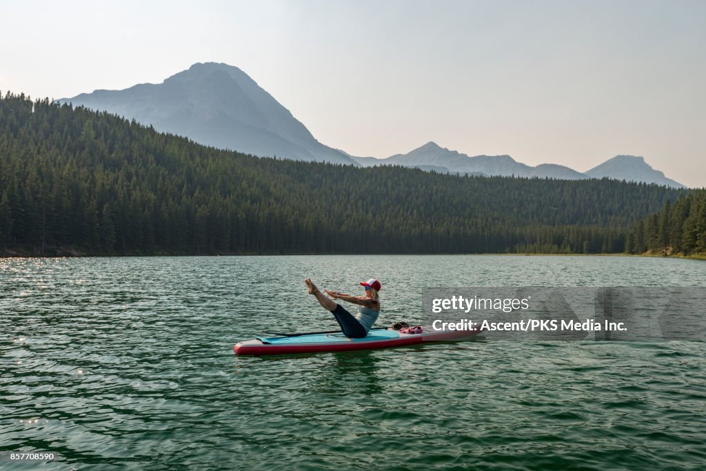 Woman performs yoga moves on paddleboard, mtn lake