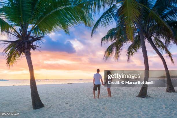 couple of tourists enjoying sunrise on a tropical beach - puesta de sol romántica fotografías e imágenes de stock