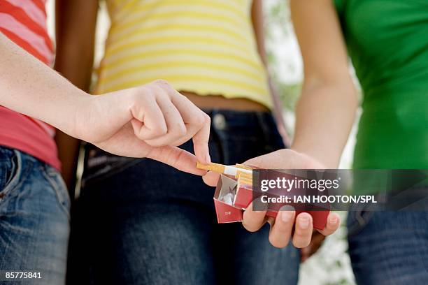 teenage girl taking cigarette from friend cigarette pack, close-up - paquete de cigarrillos fotografías e imágenes de stock