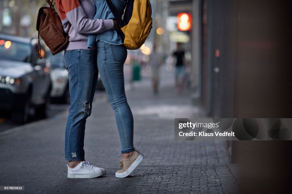 Lesbian couple, with backpacks, hugging on the street