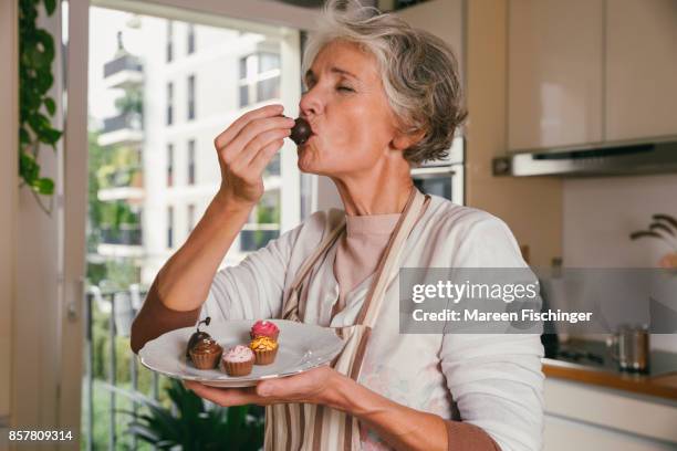 mature woman holding tasting something from her self-made mini desserts - best taste 2017 stock pictures, royalty-free photos & images