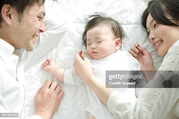 parents looking at sleeping baby, high angle view - three people bed stock pictures, royalty-free photos & images